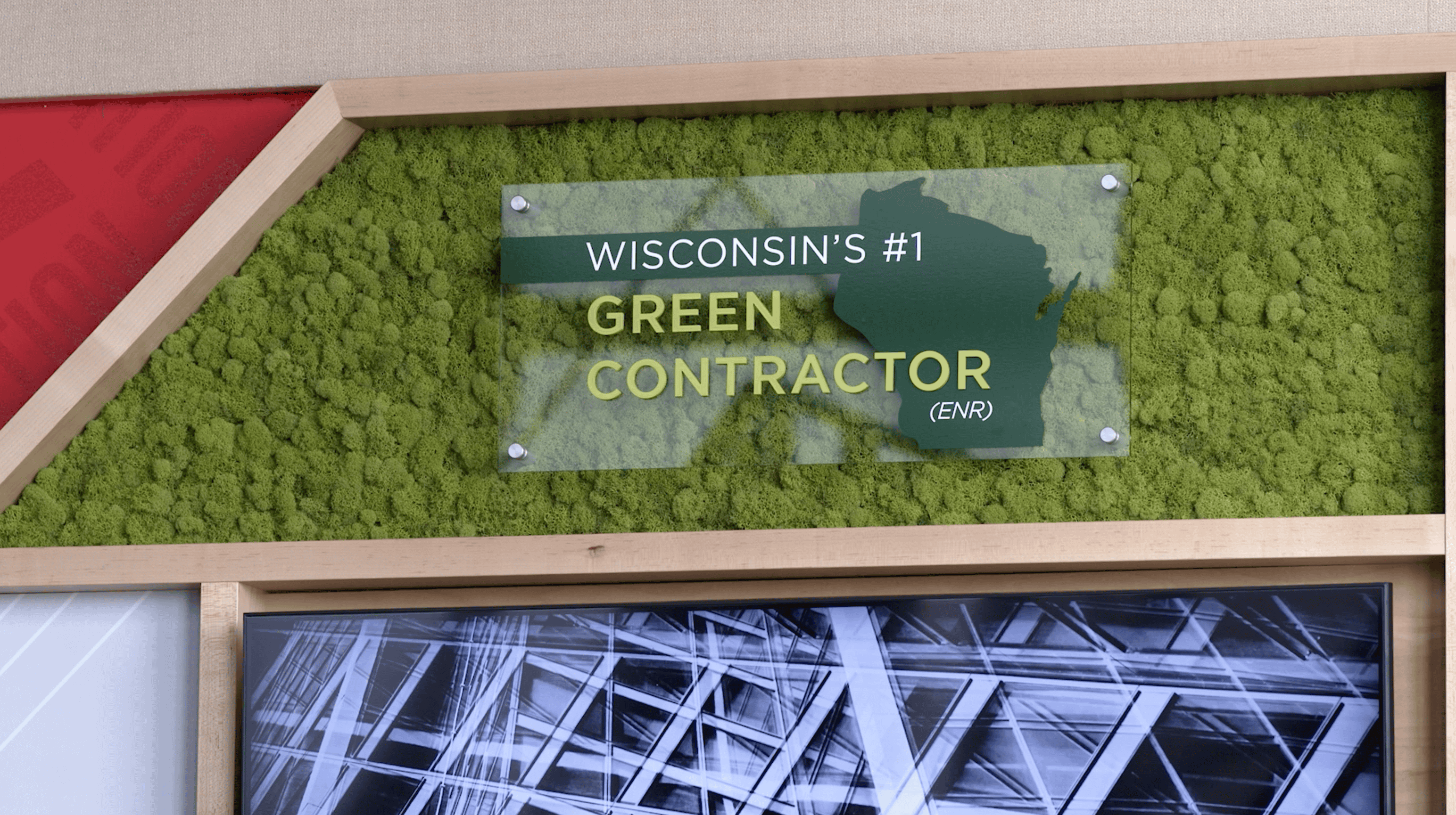 Wall display at Findorff headquarters showcasing Thysse’s facility branding work. Features green moss backdrop with a transparent sign reading 'Wisconsin’s #1 Green Contractor (ENR)' overlaid on a silhouette of Wisconsin.